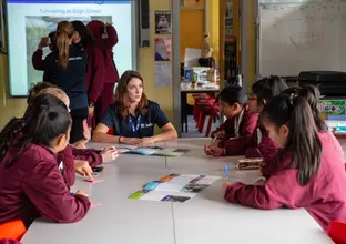 Sydney Metro staff member is sitting down and talking to a group of students at Blacktown Girls High School. 