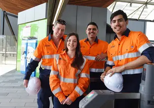 A group shot with the Infrastructure Skills Legacy Program Premier and three apprentices stood at the gate barriers at a Sydney Metro Station.