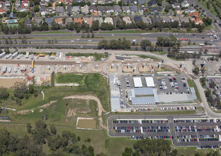 A bird's eye view of the outside of the construction progress made at Sydney Metro's Kellyville Station showing the large raised concrete pillars where the platform will be placed and surrounding suburbs, carparks and warehouses. 