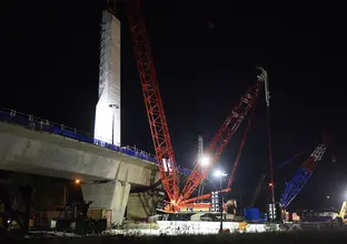 An on the ground view looking at the construction of the skytrain bridge tower as a crane lift is lifting material to the top of the tower at night at Sydney Metro's Rouse Hill. 