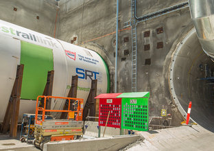 An on the ground view looking across to Tunnel Boring Machine (TBM) 4 Maria showing green in sign and red out side for the twin tunnels at a Sydney Metro construction site for the West Railway Link.