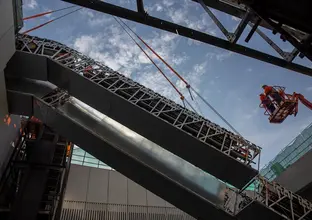 An on the ground view looking up as the double escalators are being crane lifted into place and two construction workers on a crane lift are inspecting the installation at Sydney Metro's Norwest site n May 2018. 