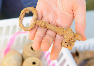 A close up image of someone holding an ancient rusty key artifact found at Sydney Metro;s White Hart Inn dig site. 