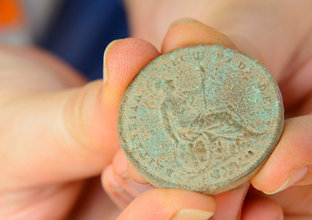 Close up view of someone holding an old copper coin that has oxidised with a green tint found at White Hart Inn archaeological site