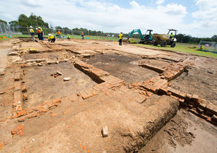 Several people in high visibility clothing are amongst the White Hart Inn archaeological site with heavy machinery in the background.