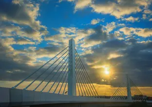 An arial view showing the completed Cable Stay Bridge with a beautiful sky as the sun peeps through a cloud in the background at Sydney Metro's Rouse Hill. 