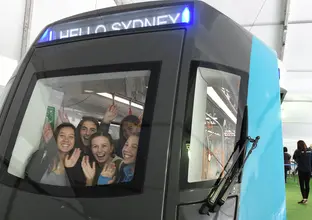 A group of five girls smiling and waving from the front of the Sydney Metro train carriage that was displayed at the Royal Easter Show. 