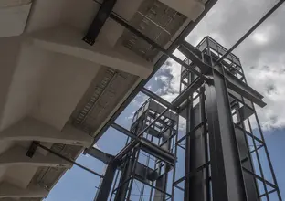 An on the ground view looking up at the construction of the two towered lift shaft sat Sydney Metro's Kellyville Station from underneath the platform concourse. 