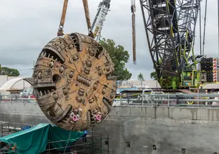 The cutterhead of a Tunnel Boring Machine (TBM) is being retrieved as it is being lifted out of the construction site by a crane as work nears completion on the Sydney Metro's Northwest project. 