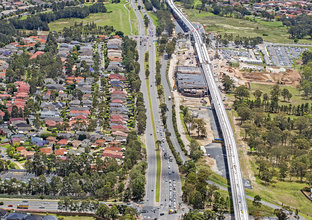 An aerial view of the new Sydney Metro skytrain bridge alongside a motorway while a suburban development is pictured to the left.