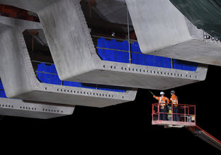 Two construction workers on a crane inspecting the bridge deck on the Windsor Road railway bridge at Sydney Metro's Rouse Hill Station. 