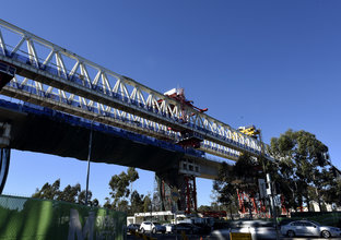 The skytrain is constructed over Samantha Riley Drive while cars drive underneath.