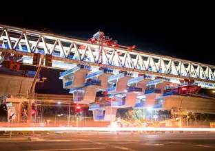 An on the ground view looking up at the construction of the final span of Sydney Metro's skytrain bridge  at night. 