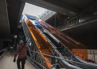 An on the ground view showing the construction of the escalators at Sydney Metro's Norwest Station as a construction worker walks past carrying material them. 