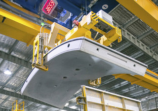 A close up shot looking up at the final concrete segment being lifted into place by the crane above. 