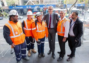 Construction workers pose with men in suits.
