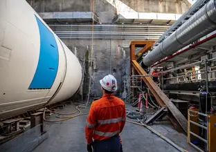 An on the ground view od a construction worker inspecting Tunnel Boring Machine Mabel in place at a Sydney Metro construction site.