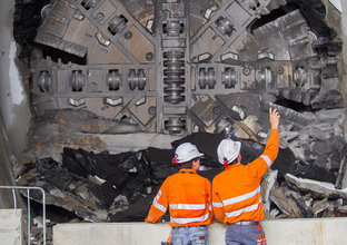 An on the ground view of two construction workers inspecting the tunnel breakthrough from Tunnel Boring Machine (TBM) 1 Elizabeth at Sydney Metro's Hills Showground Station. 