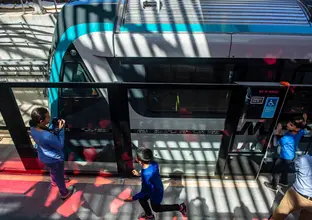 A bird's eye view of community members standing in front of the platform screen doors while a metro train approaches.