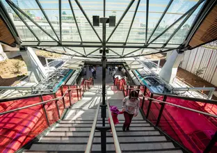 The view from the top of the stairs at Cherrybrook Station looking down to the station's platforms. A woman and a child are holding hands walking up the stairs.