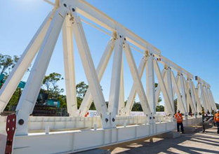 An on the ground view of three construction workers putting together the metal structure of the Gantry crane used in many Sydney Metro Construction sites. 