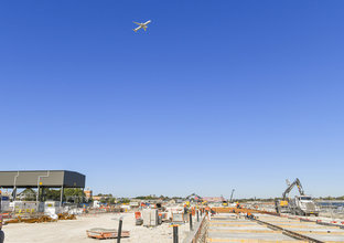 A wide angle of Sydney Metro Trains Facility South Yard under construction in Marrickville with a airplane flying above it.