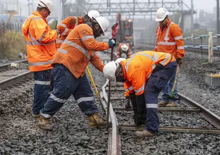 A group of construction workers in orange high-vis are placing the new metro tracks into place at Bankstown Station.