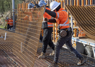Three construction workers place a sheet of metal rods in place during track works at Dulwich Hill Station.