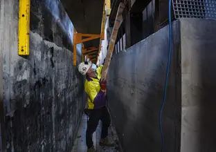 A construction worker is lifting a ladder into place while working on the building cores and internal rooms of Pitt Street Station.