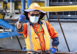 A construction worker in orange high-vis, facemask and sunglasses gives the camera a thumbs-up while on site at Waterloo Station.
