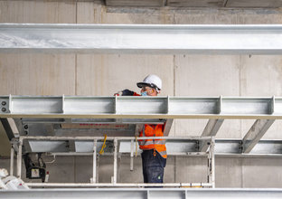 A construction worker is standing between steel beams while installing them at Waterloo Station. 