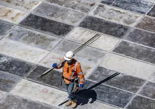 A birds eye view of a construction worker walking with metal rods over his shoulder.