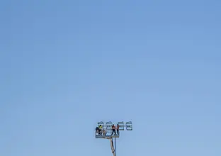 Three construction workers are on top of a tall crane with a clear blue sky in the background.