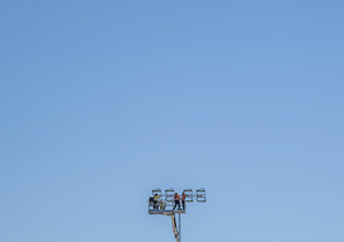Three construction workers are on top of a tall crane with a clear blue sky in the background.