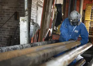 Construction worker wearing a helmet, face mask and PPE suit, pulling a metal pipe.