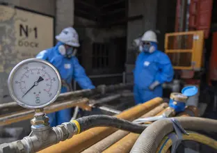 A close up view of a pressure gauge while two men in full PPE suits are in the background.