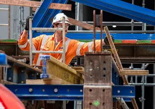 Construction worker on a ladder pulling metal rods on top of a steel metal frame at Sydney Metro's Waterloo Station.