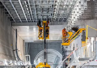 Two construction workers standing on a cherry picker lift while installing the ceiling inside Victoria Cross Station.