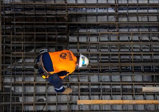 A construction worker bends over using a hand drill on the metal track supports inside Sydney Metro's Victoria Cross station.