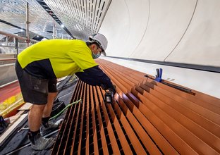 A construction worker bends over using a hand drill while working inside the cavern at Sydney Metro's Victoria Cross station.