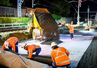 Truck emptying dirt and construction workers laying track at Sydney Metro's Chatswood Station.