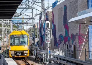 Colourful aboriginal artwork covers the brick ventilation buildings along the tracks at Central Station while a yellow train is approaching the platform.