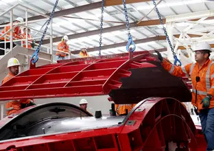 Two men in high visibility are guiding a precast mould segment.