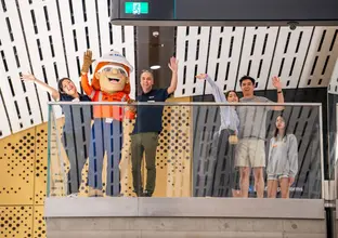 People standing with the mascot with their hands in the air