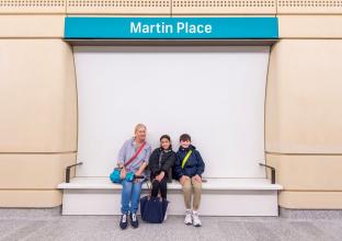 Mother and two children sitting in front of a Martin Place sign in the station