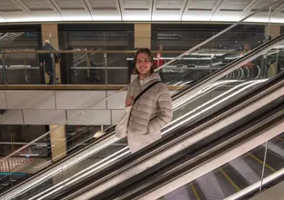 Member of the community in a light coloured puffer jacket going down the escalator