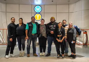 Group of people gathered for a photo in front of M and T neon signs