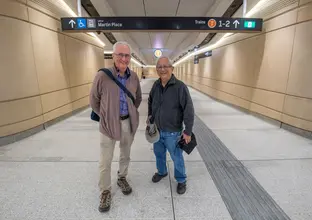 Two elderly men standing in front of directory signs in the station