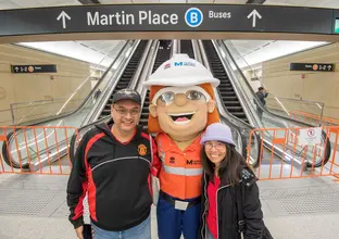 Couple with the Metro Mascot in front of the escalators on the platform