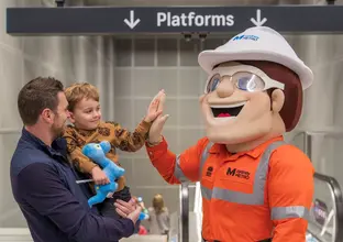 Dad holding son high fiving the Sydney Metro mascot